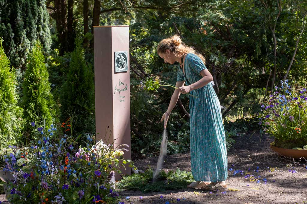 Ein Mädchen wirft Erde in das Grab vom Opa nach dem die Urne beigesetzt wurde, Bestattung Berlin Pankow.